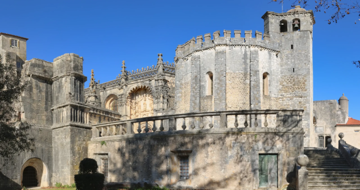 The Convent of Christ seen from the garden: the round Templar rotunda, crowned with battlements, adjoining the Manueline church and its balustraded terrace.